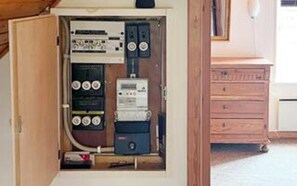 An electrical panel with various switches and meters, a wooden cabinet, and a white appliance in the background. - 6 Person Holiday Home in Aeroskobing (Aeroskobing)