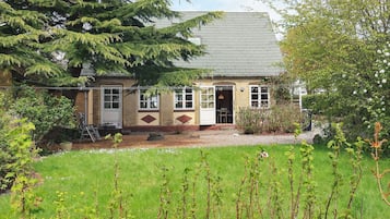 A two-story house with a front door, a small porch, and a garden with grass and plants.