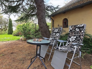 Une terrasse avec deux chaises et une table, entourée de verdure et bordée d’un bâtiment dont le toit est recouvert de tuiles.