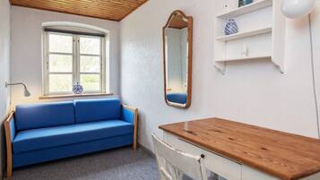A room with a blue sofa, a wooden table, a chair, a window, a mirror, and a shelf with decorative items.