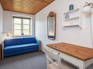 A room with a blue sofa, a wooden table, a chair, a window, a mirror, and a shelf with decorative items. - 6 Person Holiday Home in Aeroskobing (Aeroskobing)
