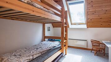 Habitación con literas, un escritorio y una silla de mimbre, con tragaluz.