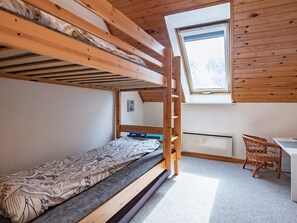 Habitación con literas, un escritorio y una silla de mimbre, con tragaluz.