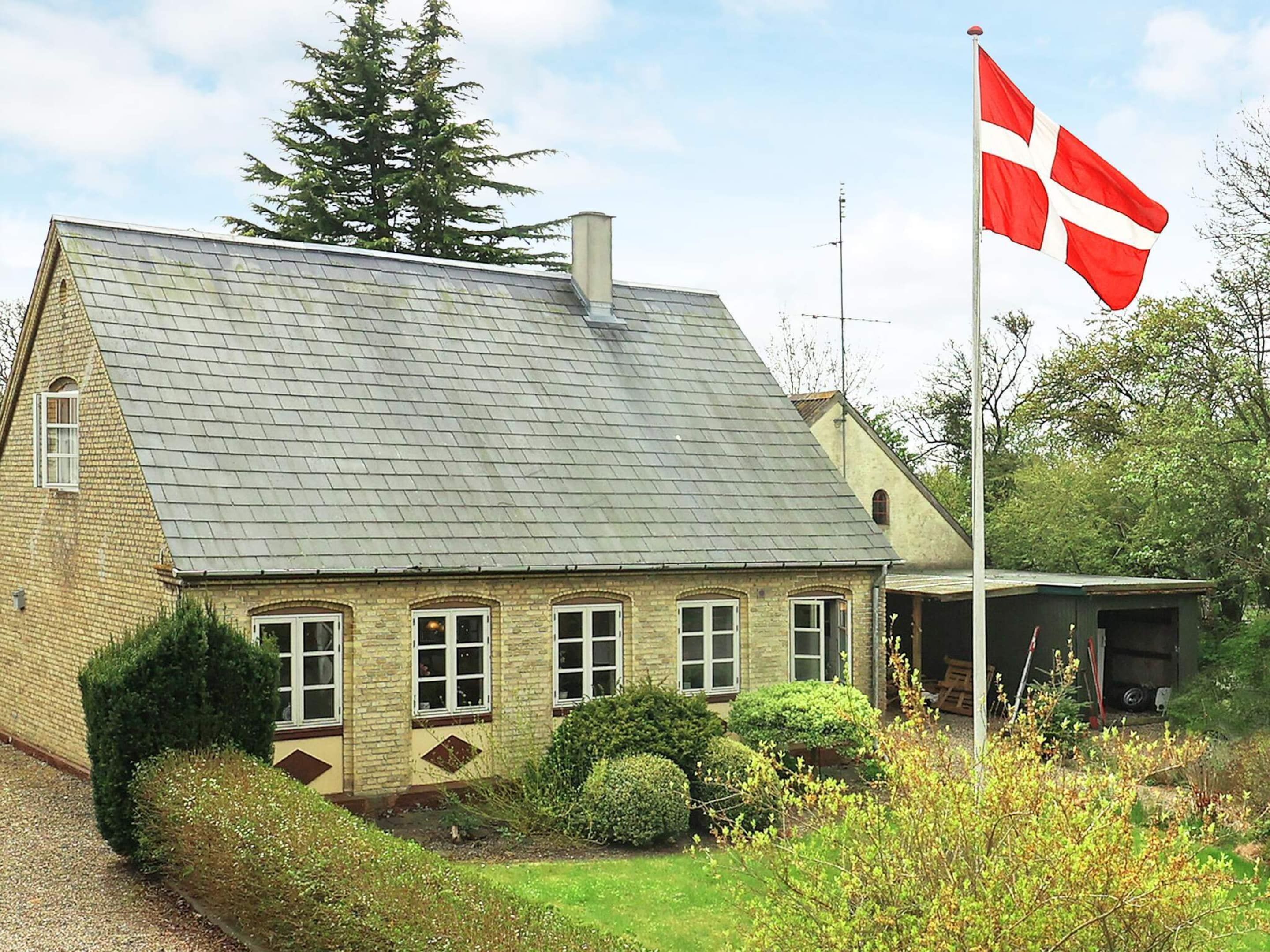 A traditional brick house with a sloped roof, a flagpole with a flag, and well-maintained hedges.
