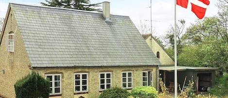 A traditional brick house with a sloped roof, a flagpole with a flag, and well-maintained hedges.