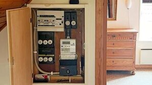 An electrical panel with various switches and meters, a wooden cabinet, and a white appliance in the background. - 6 Person Holiday Home in Aeroskobing (Aeroskobing)
