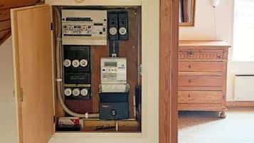 An electrical panel with various switches and meters, a wooden cabinet, and a white appliance in the background.