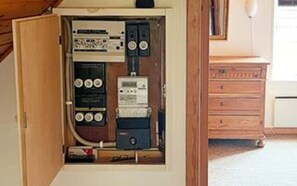 An electrical panel with various switches and meters, a wooden cabinet, and a white appliance in the background. - 6 Person Holiday Home in Aeroskobing (Aeroskobing)