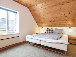 Un dormitorio con techo inclinado, una cama con colchón acolchado, dos lámparas de noche y una ventana con vistas a un tejado de baldosas.