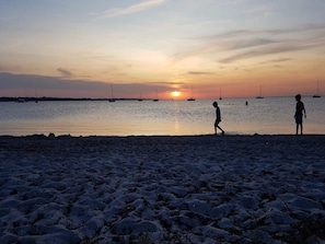 Una playa al atardecer con barcos a lo lejos.