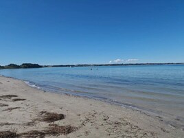 Una playa con agua cristalina, una orilla arenosa y formaciones terrestres a lo lejos.