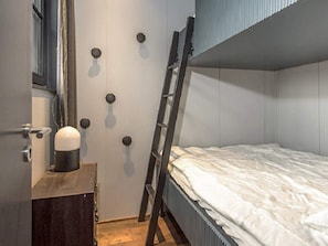 Une chambre avec un lit superposé, une échelle appuyée contre le mur, une petite armoire en bois et une porte dotée de poignées rondes.