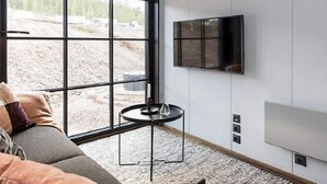 A modern living room with a large window, a sofa, a small round table, and a mounted television. - 4 Star Holiday Home in Salen (Salen)