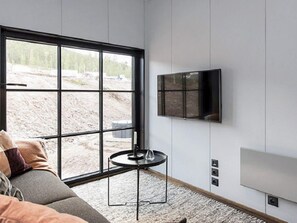 Un salon moderne avec une grande fenêtre, un canapé, une petite table ronde et un téléviseur fixé au mur.