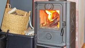 Un poêle à bois avec une flamme visible à l’intérieur, un panier de bois de chauffage et une boîte de rangement noire.