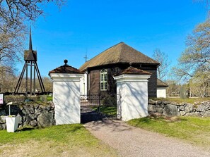 En kyrka med ett torn, en stenmur och en grusgång som leder fram till ingången.