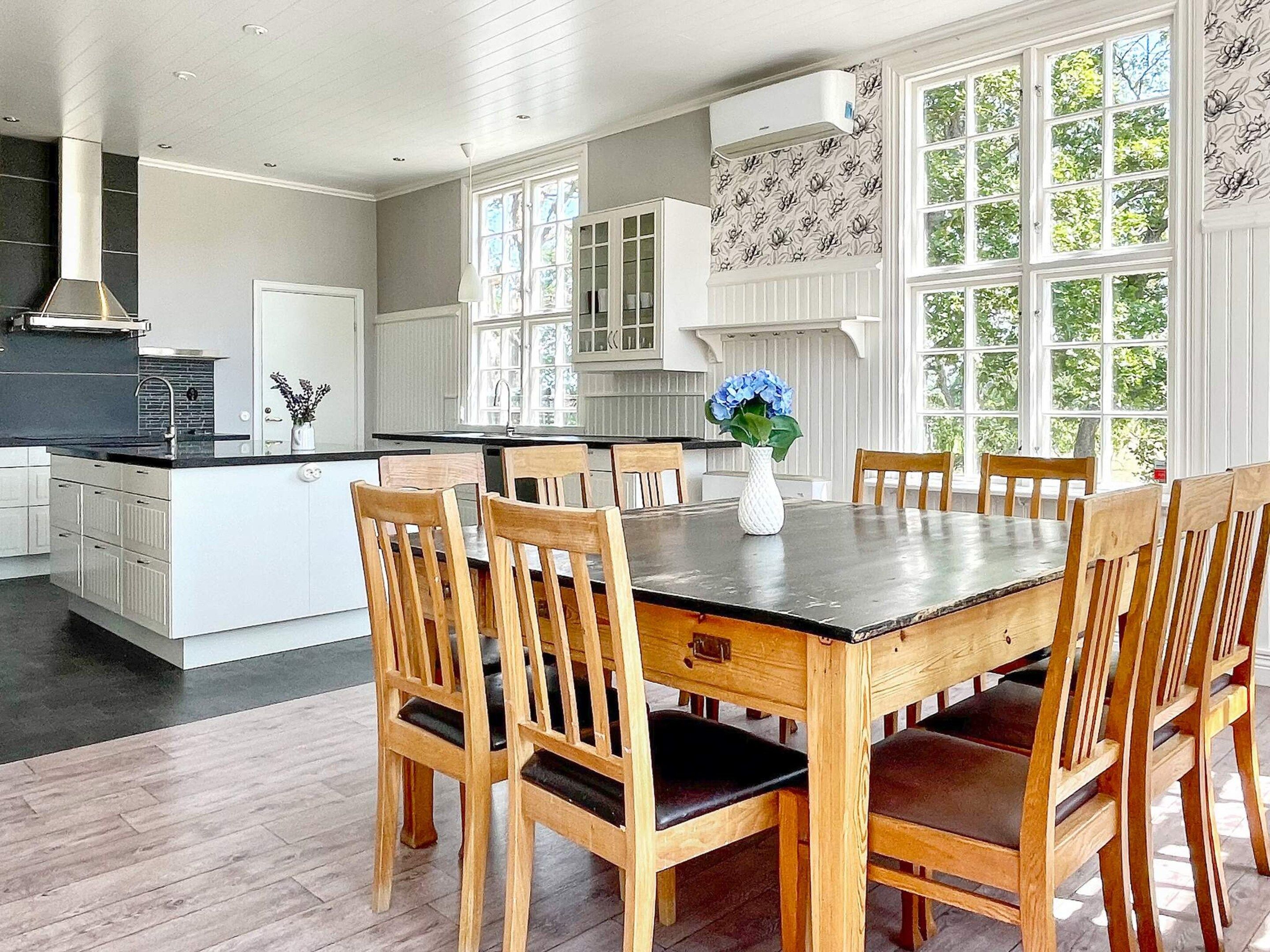 Una cocina moderna con armarios blancos, una isla central y un comedor con sillas y mesa de madera.