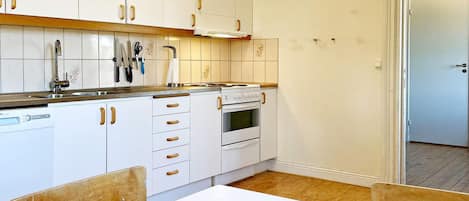 A kitchen with white cabinets, a dishwasher, an oven, and a table with chairs.