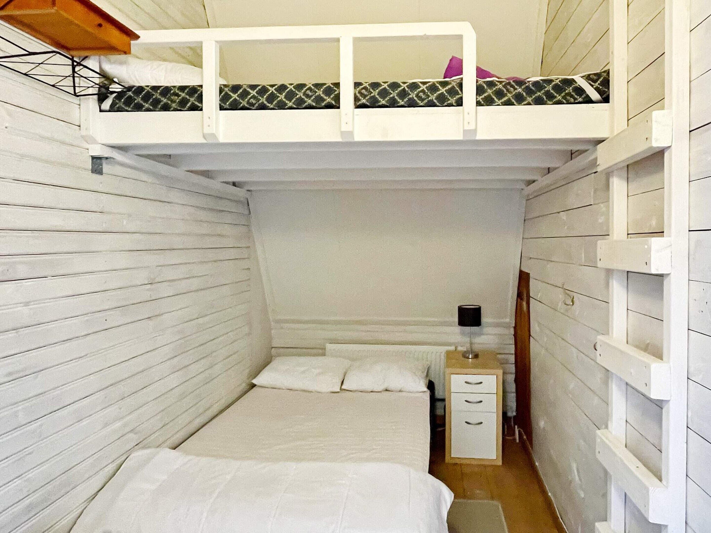 A narrow room with a bunk bed, a single bed, a bedside table, and a lamp.