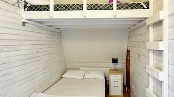A narrow room with a bunk bed, a single bed, a bedside table, and a lamp.