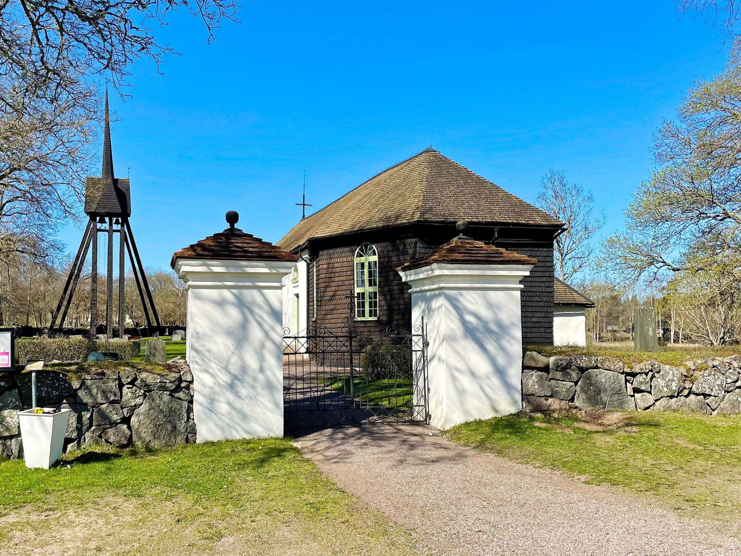 Una iglesia con campanario, un muro de piedra y un camino de grava que lleva a la entrada.