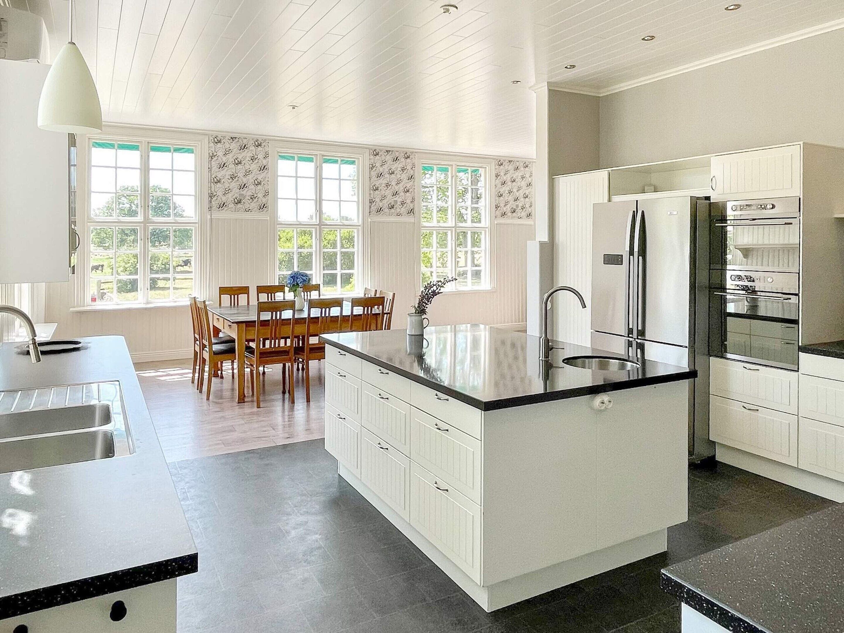 A modern kitchen with white cabinetry, a central island, and a dining area with wooden chairs and a table.