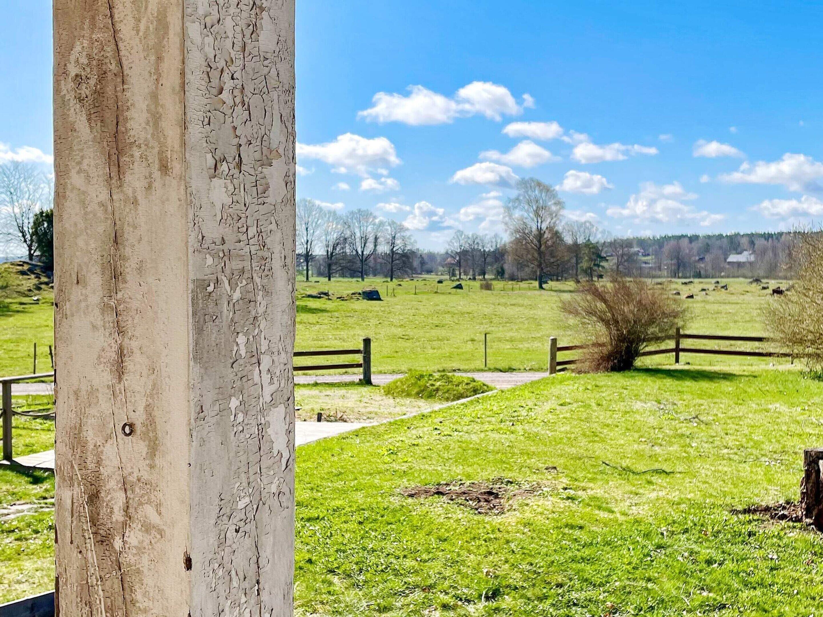 A rural landscape with a wooden fence, a grassy field, and a clear sky.