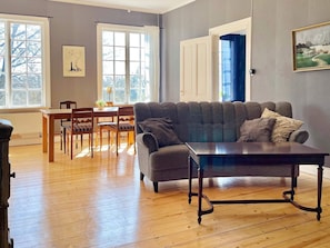 A living room with a sofa, a dining table with chairs, a window, and a painting on the wall. - 4 Star Holiday Home in Morlunda (Mörlunda)