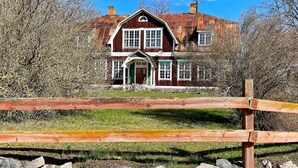 A two-story house with a prominent chimney, a front porch, and a wooden fence in the foreground.