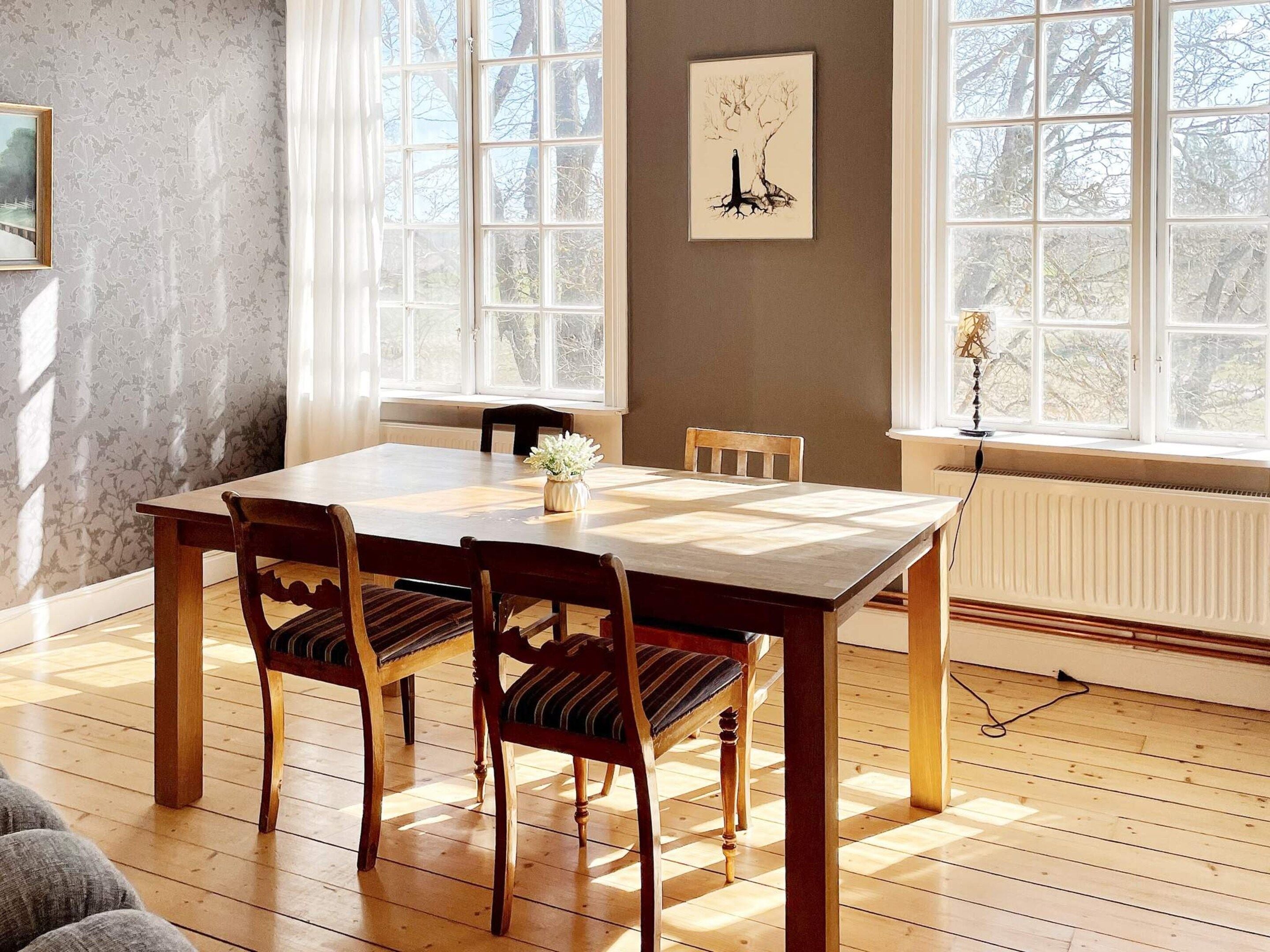 Una sala da pranzo con un tavolo e sedie in legno, un termosifone e una finestra vista alberi.