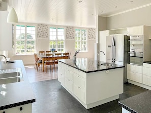 A modern kitchen with a central island, white cabinetry, and a dining area with wooden chairs and a table.
