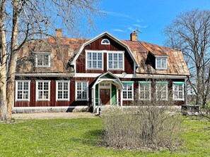 Ett tvåvåningshus byggt av trä, med en grön dörr, flera fönster och en skorsten.