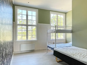 A room with bunk beds, large windows, and a radiator.