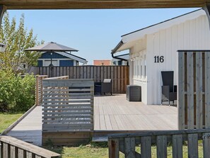 A wooden deck with outdoor furniture, a white building with the number 116, and a covered area with a table and chairs.