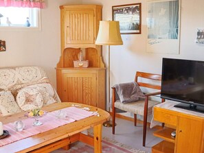 Uma sala de estar aconchegante com um sofá de madeira, uma mesa de madeira com uma luminária, uma televisão e um armário.