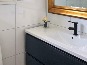 A bathroom with a white sink, black faucet, and a small vase with flowers. - 6 Person Holiday Home in Korssund (Fjaler)