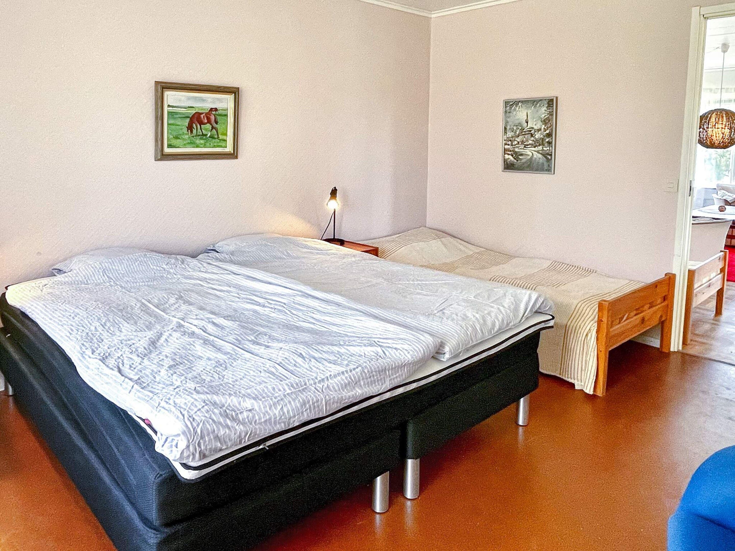 Un dormitorio con una cama doble, una mesita de noche, una lámpara y dos cuadros en la pared.