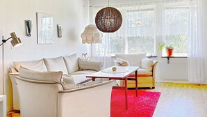 A modern living room with a sofa, a coffee table, and a chair. There is a red rug on the floor, and a window with a view of trees. - 6 Person Holiday Home in Borgholm (Borgholm)
