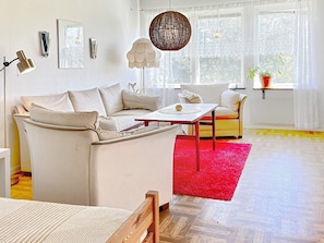 A modern living room with a sofa, a coffee table, and a chair. There is a red rug on the floor, and a window with a view of trees. - 6 Person Holiday Home in Borgholm (Borgholm)
