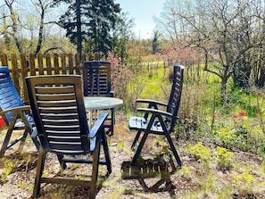 Un espacio al aire libre con sillas y una mesa, rodeado por una cerca de madera y follaje.