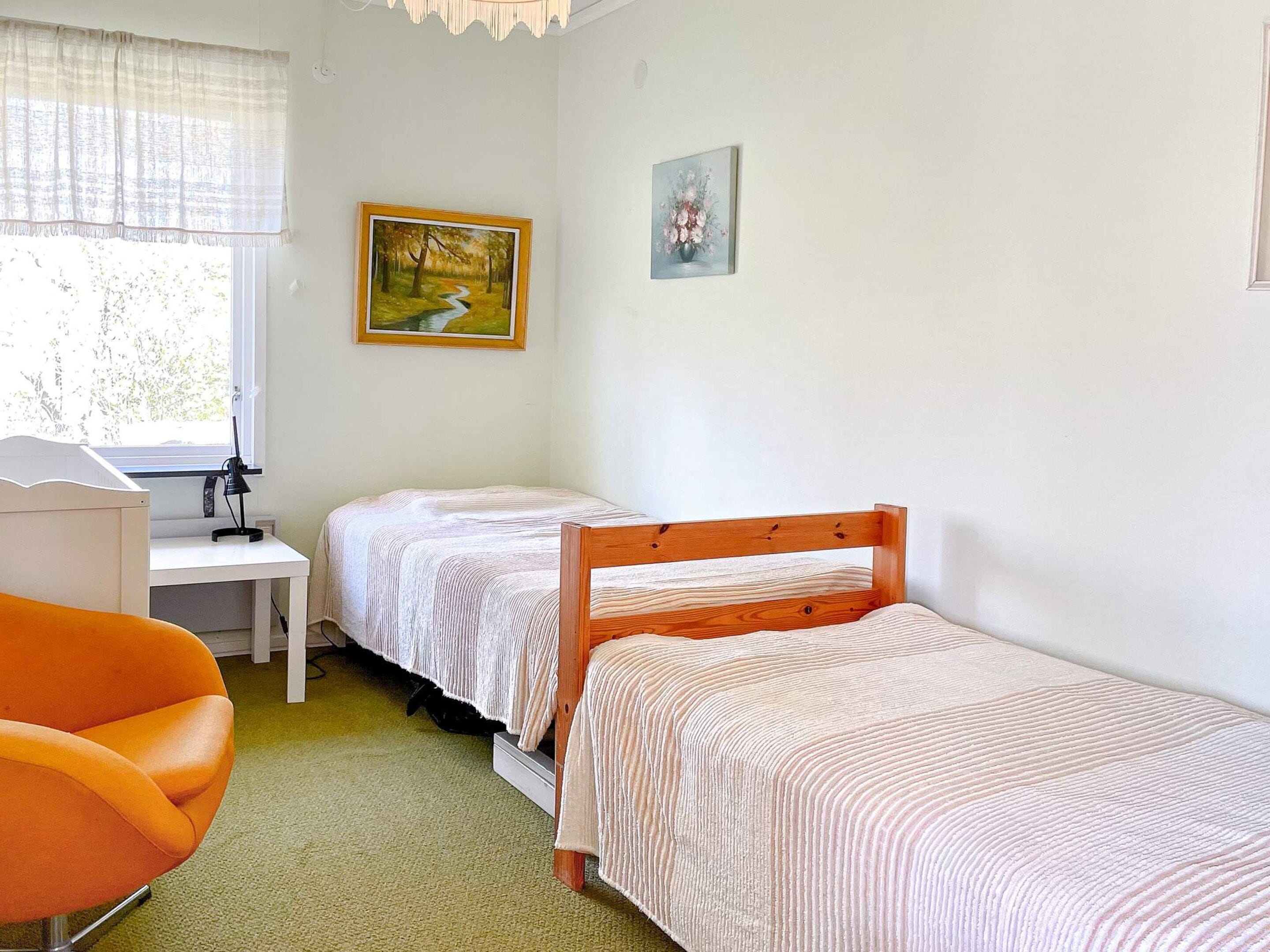 Een slaapkamer met twee eenpersoonsbedden, een bureau, een stoel en twee ingelijste foto's aan de muur.