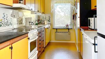 A compact kitchen with yellow cabinets, a stove, a microwave, and a window with a view of trees.