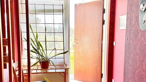 A room with a wooden chair, a potted plant, a red door, and a window with blinds. - 6 Person Holiday Home in Borgholm (Borgholm)