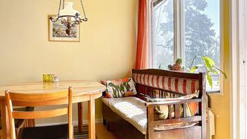 Una habitación acogedora con una mesa de madera, sillas, un banco con cojines, una lámpara colgante y una ventana con cortinas.