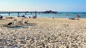 Una spiaggia con un molo che si estende nell'acqua, lettini e persone che si godono il mare.