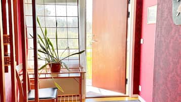 Una habitación con una silla de madera, una planta en maceta, una puerta y una ventana con persianas.