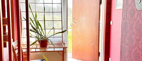 A room with a wooden chair, a potted plant, a door, and a window with blinds.