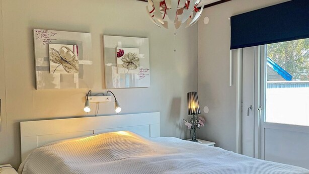 Une chambre à coucher comprenant un lit, des lampes de chevet, une table de chevet, une lampe fixée au mur et des œuvres d’art.