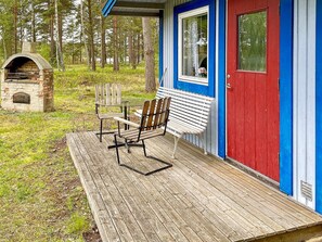 Une terrasse en bois avec un banc et une table, une cheminée en pierre et un bâtiment avec une porte rouge et des bordures bleues.