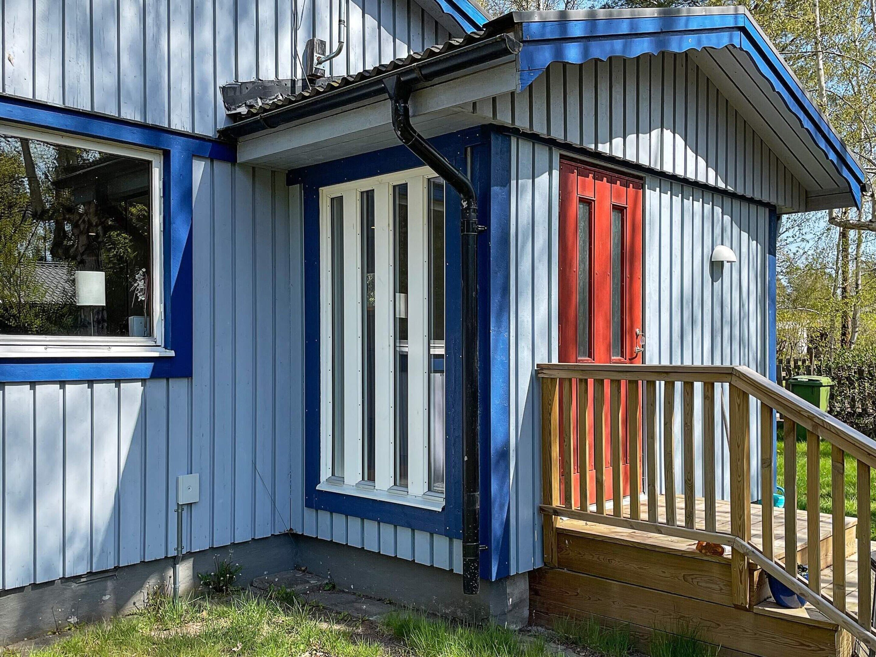 A building with a blue and white exterior, a red door, and a wooden deck.